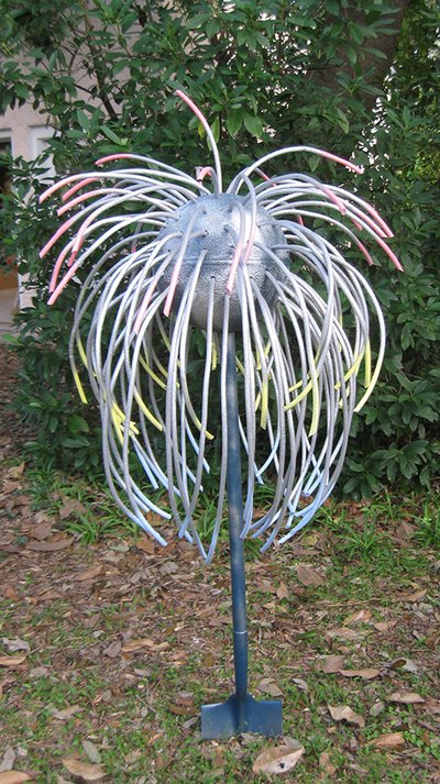 A sliver metal sphere with red, yellow and blue faded thin foam tubes hanging out of it. Its base is a shovel.