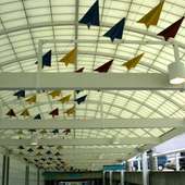 Colorful powder coat painted aluminum airplanes flock in a curve along the ceiling.