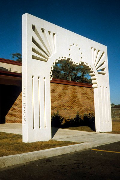 The precast concrete archway sculpture is white with cutout sections that emphasize it's height and the interior curve.