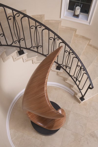 The tall laminated wood sculpture fits in a space created by a circular staircase.