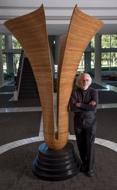 David Engdahl stands next to the large laminated wood sculpture that shows how the sculpture is split down the middle.