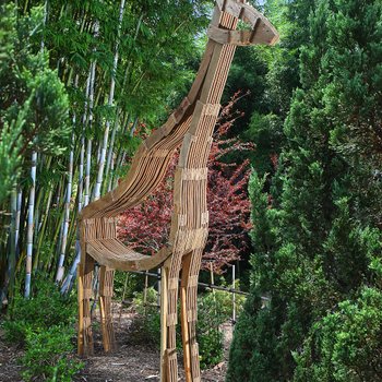 Lifesize stylized rough plywood giraffe stands tall amongst the landscape at the zoo.